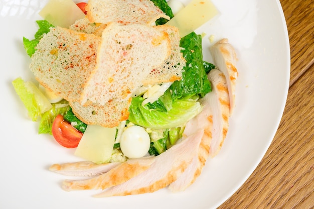 Caesar salad with croutons, quail eggs, cherry tomatoes and grilled chicken in wooden table.Delicious salad with chicken, nuts, egg and vegetables.