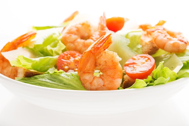 Caesar salad with fresh leaves, shrimp, cherry tomatoes in a plate isolated on a white background. Close-up