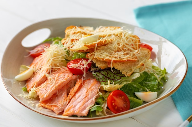 Caesar salad with grilled chicken on white wooden background