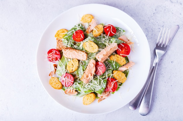 Caesar salad with red fish (salmon, trout), cherry tomatoes, croutons, parmesan cheese and romaine. Traditional American dish. Close-up, selective focus, top view.