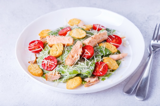 Caesar salad with red fish (salmon, trout), cherry tomatoes, croutons, parmesan cheese and romaine. Traditional American dish. Close-up, selective focus.