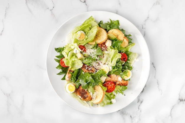 Caesar salad with roasted chicken meat tomatoes croutons and parmesan cheese in white plate