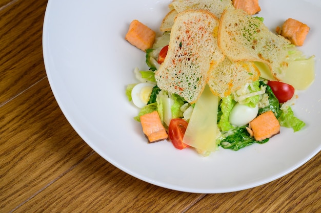 Caesar salad with salmon on white plate on wooden background.Caesar salad with salmon,top view