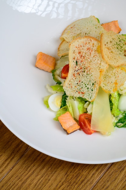 Caesar salad with salmon on white plate on wooden background.Caesar salad with salmon,top view