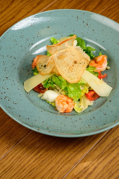 Caesar salad with shrimp on blue plate on wooden background.Caesar salad with shrimps,top view