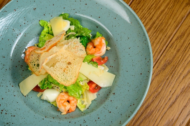 Caesar salad with shrimp on blue plate on wooden background.Caesar salad with shrimps,top view