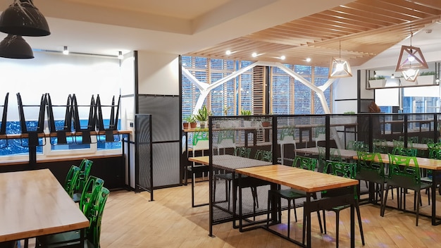 Cafeteria, no people dining room with wooden tables and green chairs. Interior with wood and metal elements. Modern dining areas with window lighting. Ukraine, Kiev - February 19, 2021.