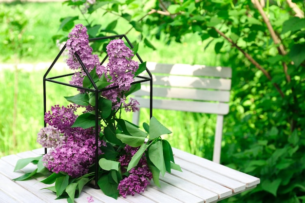 Cage with beautiful lilac flowers on table in garden