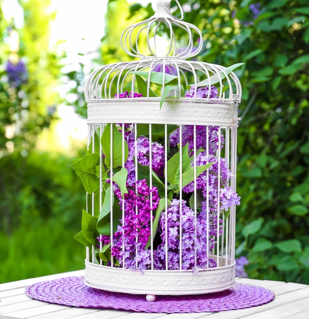 Cage with lilac flowers on table in garden