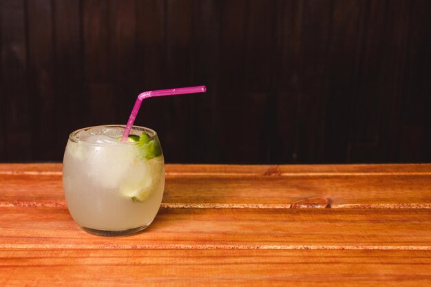 Caipirinha cocktail in a glass tumbler on a wooden table with copy space.