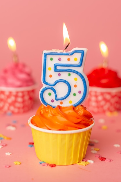 Photo cake for the fifth birthday candle number 5 in a cupcake among colorful cakes on a pink background