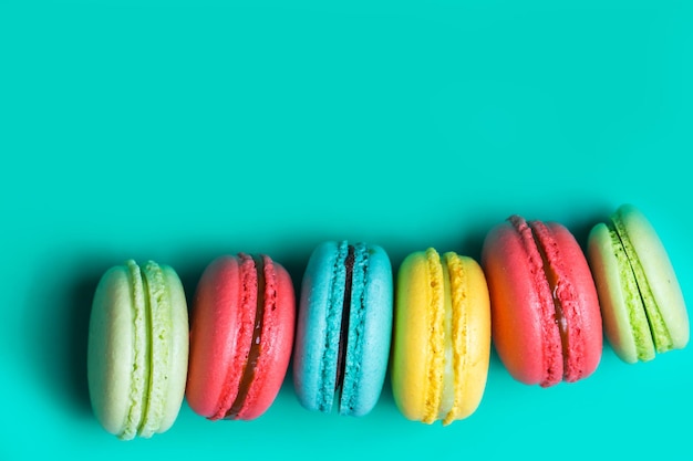 Cake a lot of colorful french cookies macarons on turquoise background with copy space