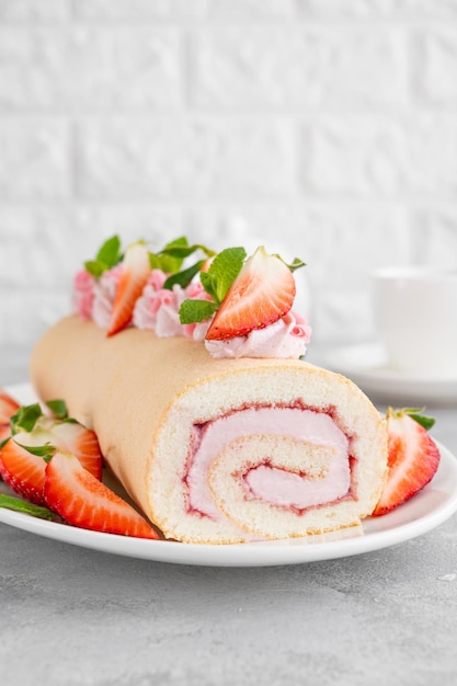 Cake roll with fresh strawberries jam and cream cheese on a white plate on a gray background