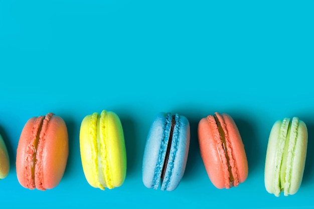 Cake sweet macaron or macaroon on blue background with copy space, pastel colors, top view. Yellow, coral, green French pastries, Breakfast