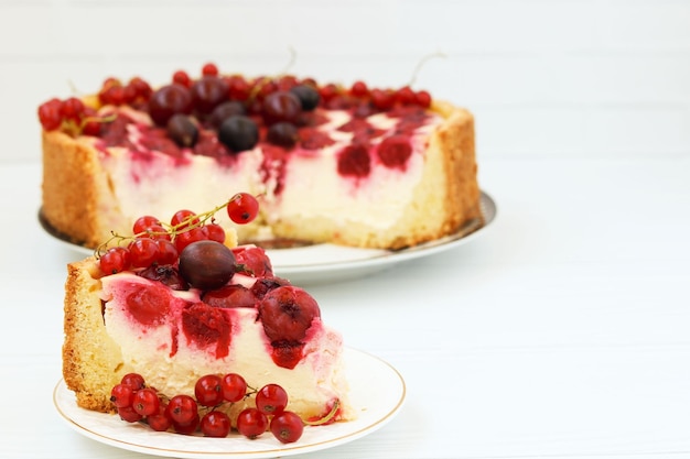 Cake with berries is located on a plate on a white background piece of cake in the foreground