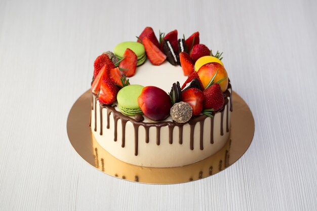 Cake with chocolate drips, strawberries, peaches, macaroons, rosemary and Oreo