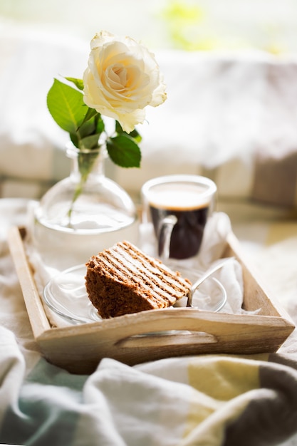 Cake with coffee and flower in tray on bed