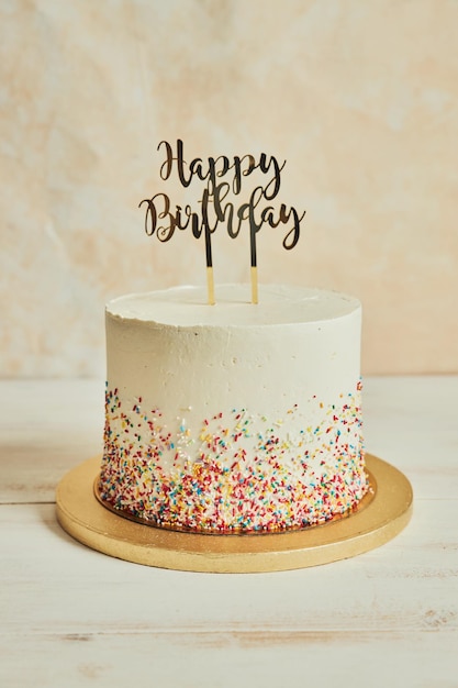 Cake with a ''happy birthday'' cake topper and sprinkles on a wooden board on the table