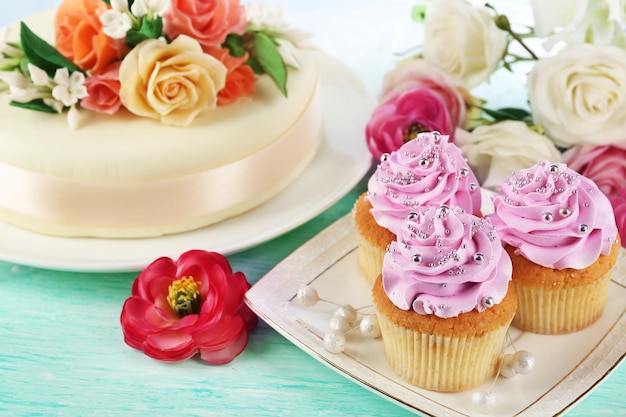 Cake with sugar paste flowers and cupcakes on light background