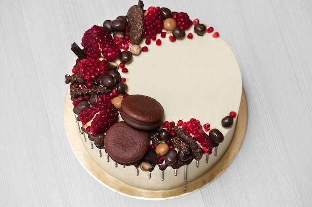 Cake with white cream, chocolate drips, pomegranate, nuts and chocolate decor