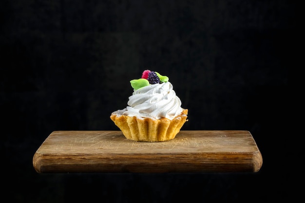 Cake with white cream decorated with berries on a wooden board on a black background