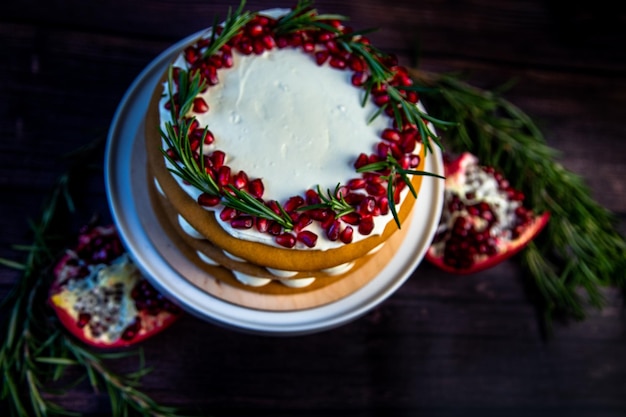 Cake with white cream and honey brown cakes lies on a white stand decorated with pomegranate and ros...