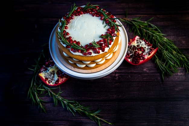 Cake with white cream and honey brown cakes lies on a white stand decorated with pomegranate and ros...