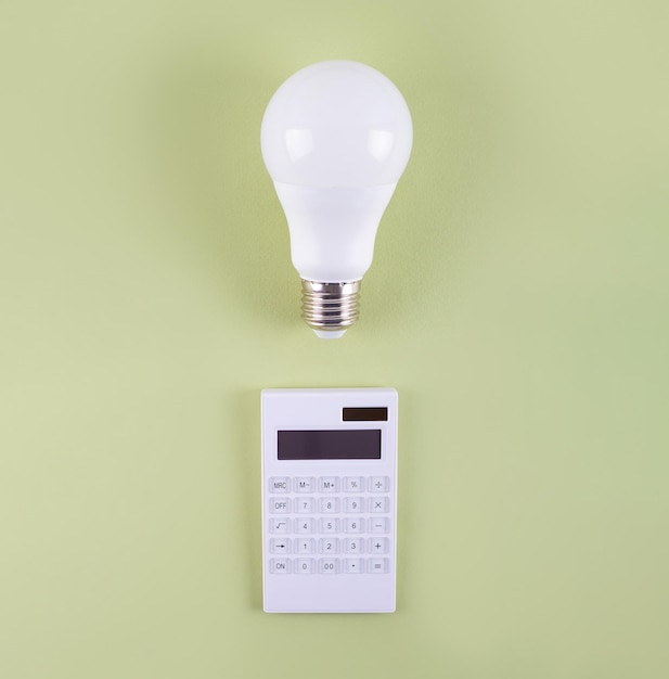 Calculation of electricity costs Calculator and energysaving light bulb on a olive background