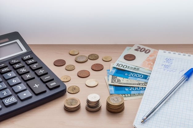 Calculator, coins, banknotes, money, a notebook, a pen on the desk