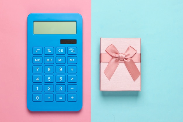 Calculator and gift box with bow on pink blue pastel. Calculation of the value of the gift.