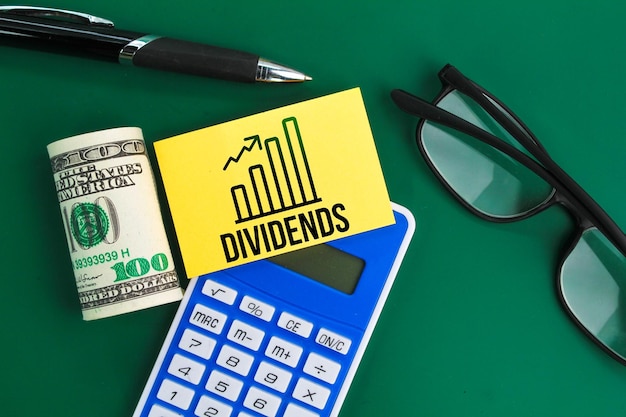 calculator glasses pen and paper money with the word dividend the concept of DIVIDENDS