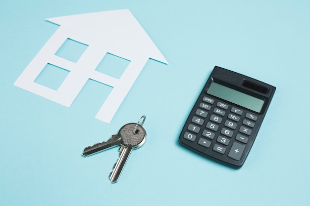 Calculator and keys with paper cutout of house over backdrop