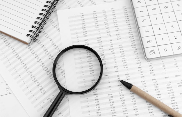 Calculator magnifying glass and notebook lying on financial statement