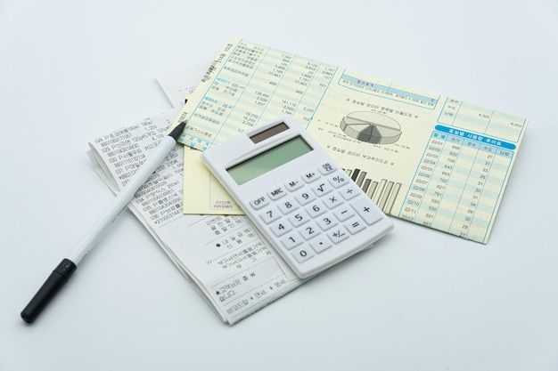 A calculator and a pen are on top of a pile of papers.