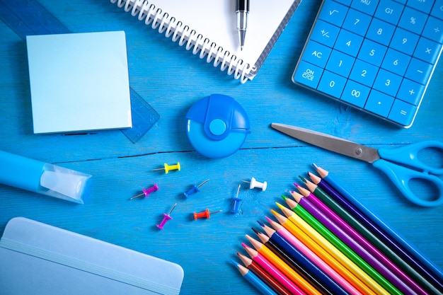 Calculator pencils note eraser scissors pen sticky notes on the blue background