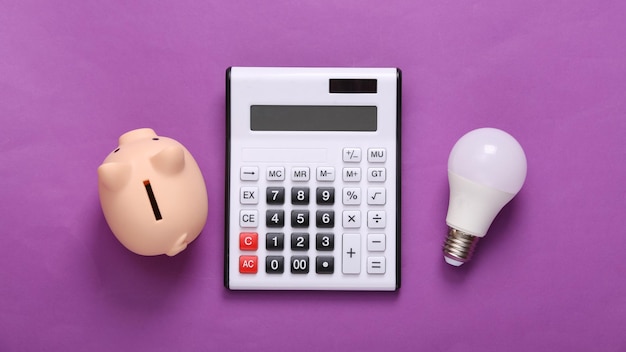 Calculator and piggy bank light bulb on purple background Top view