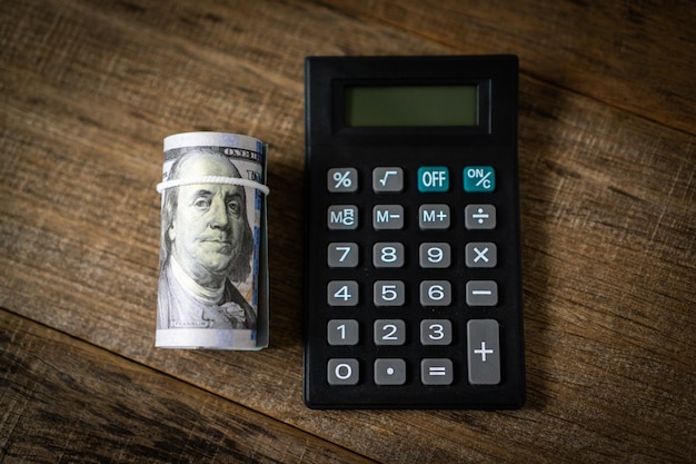 A calculator and a roll of dollar banknote.