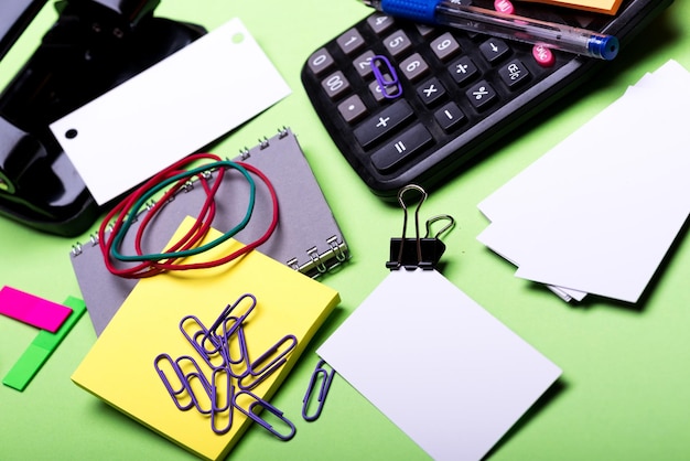 Calculator and stationery Office tools on green background close up Notebook in grey color hole punch business cards sticky notes elastics and clips Business and office work concept