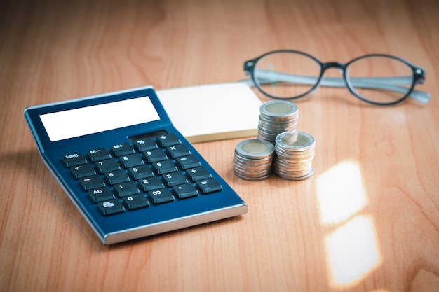 A calculator with blank screen on the table, next to money and glasses