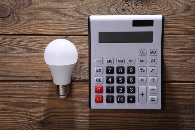 Calculator with light bulb on wooden background Top view