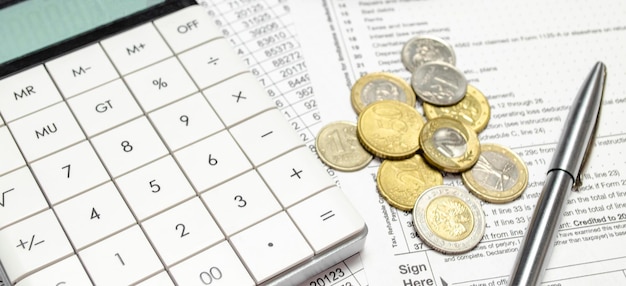 Calculator with stack of coins and pen on papers