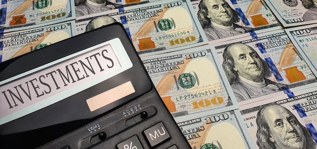 A calculator with the word investments on the screen against a background of many 100 bills