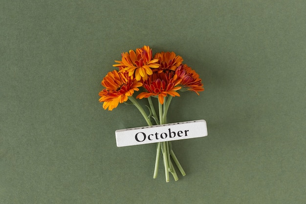 Calendar autumn month October and orange flowers on green background. Top view Flat lay. Minimal concept Hello fall. Template for your design, greeting card