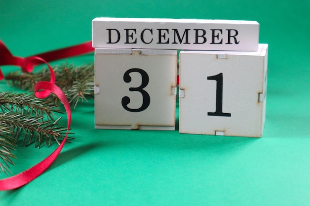 Calendar numbers 3 and 1 on cubes with spruce branches red ribbon on a green background side view closeup