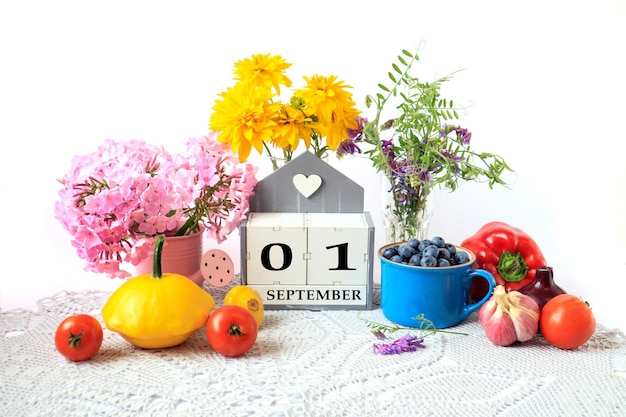 Calendar for September 1 the name of the month in English cubes with the numbers 0 and 1 ripe vegetables bouquets of various flowers blueberries in a blue cup on a gray napkin white background