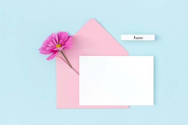 Calendar summer month June white blank card pink envelope and flowers on blue background Minimal style Top view Flat lay Mockup