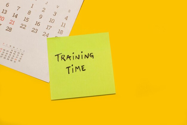 Photo a calendar with a sticky paper with training time phrase written on it on a yellow background