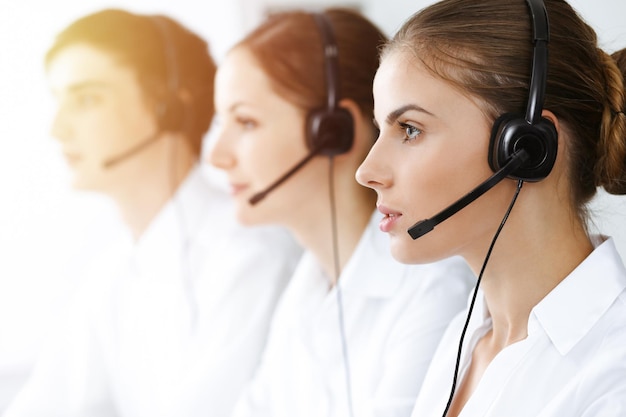 Call center. Beautiful young woman using headset and computer to help customers in sunny office. Business concept.