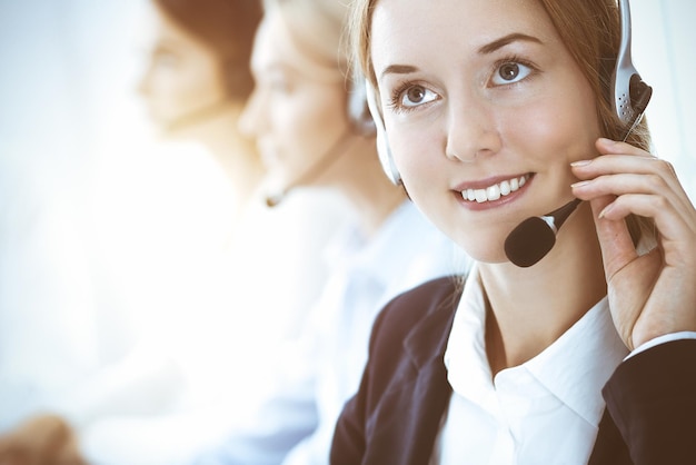 Photo call center and business people concept. beautiful business woman with headphones consulting clients. group of diverse phone operators at work in office.