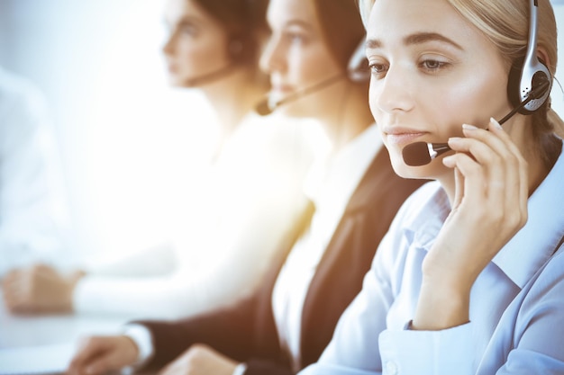 Photo call center and business people concept. beautiful business woman with headphones consulting clients. group of diverse phone operators at work in office.